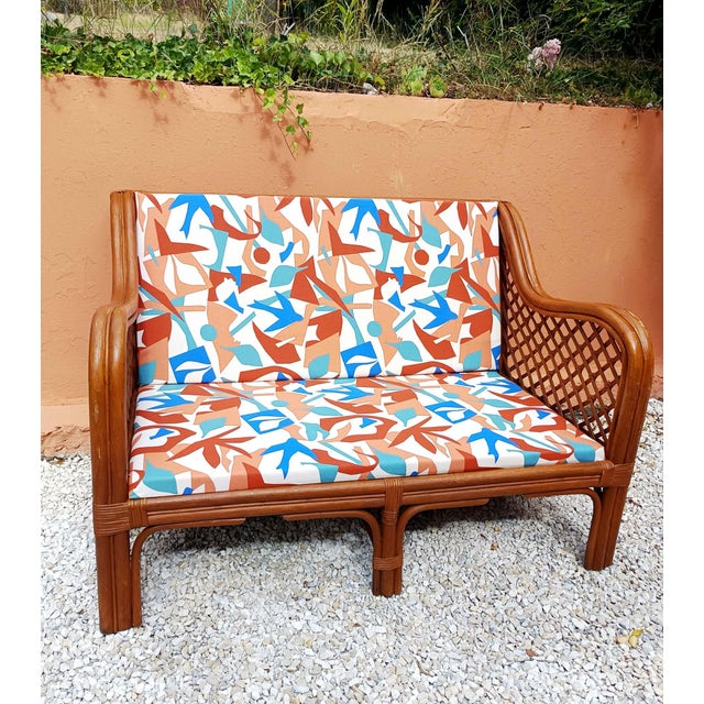 Two-seater rattan sofa/bench in a honey color, vintage design circa 1970. Armrests with a cross-braced design. The seat...