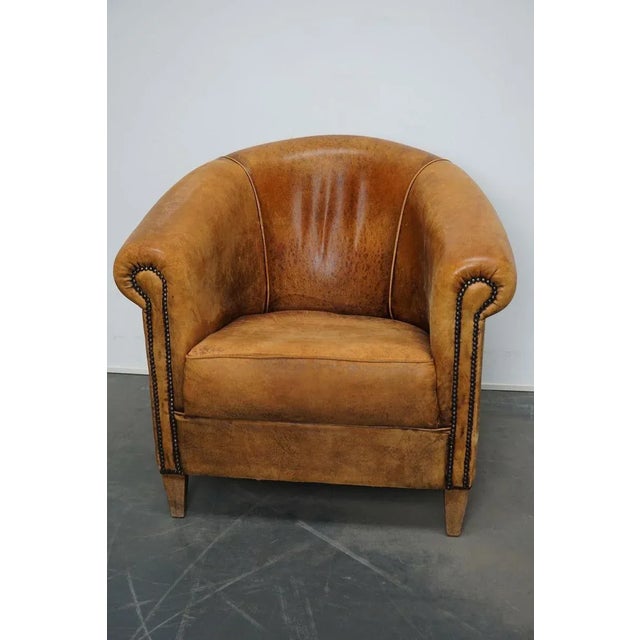 This vintage club chair is upholstered with cognac-colored leather and features metal rivets and wooden legs.