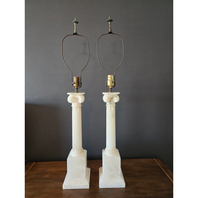 Elegant pair of carved alabaster column lamps in the Neoclassical Revival style. Features fluted pillars and Ionic-style...
