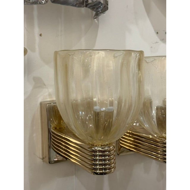 The product is a pair of Murano gold glass cup sconces, which are decorative lighting fixtures that can add a touch of...