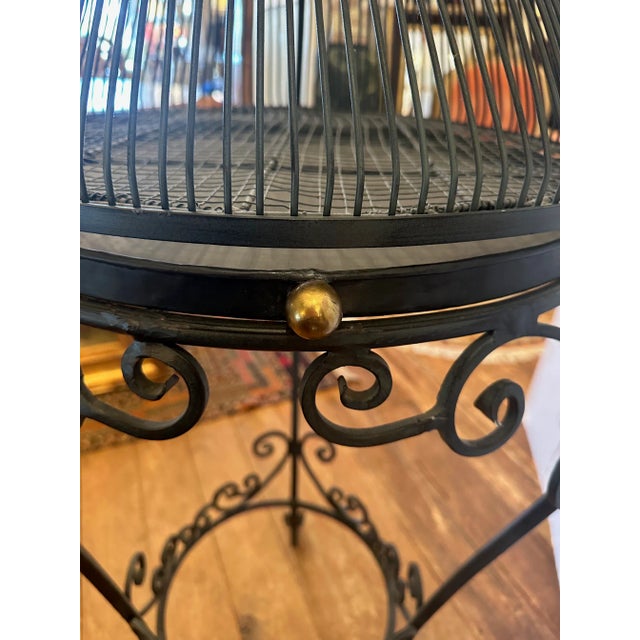Striking and unusual whimsical black iron standing birdcage having 2 perches, removable round tray, and brass ball knob on...