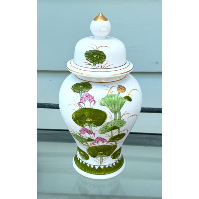 Vintage Lotus Ginger Jar with Gilded Finial Features a hand-painted lotus blossom motif in soft blush, sage, and verdant...