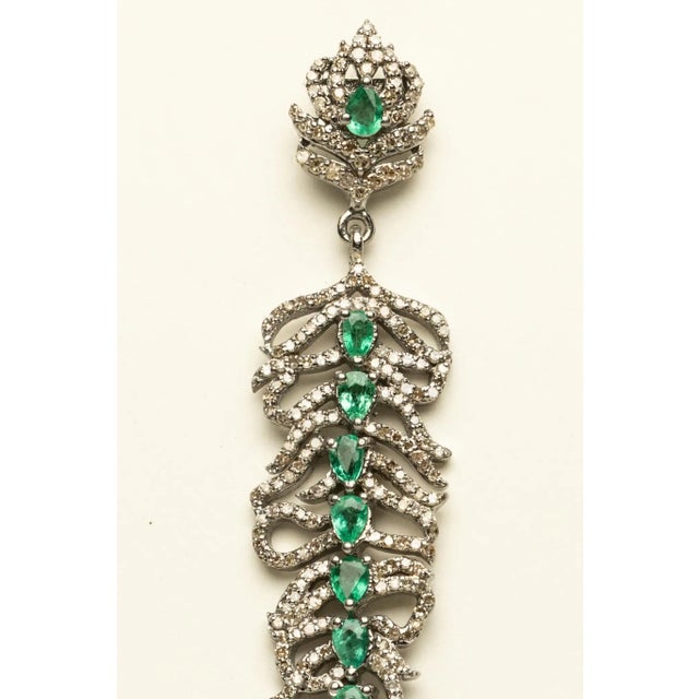 A pair of long dangle earrings with a line of faceted oval emeralds down the spine totaling 2.24 carats. Surrounding the...