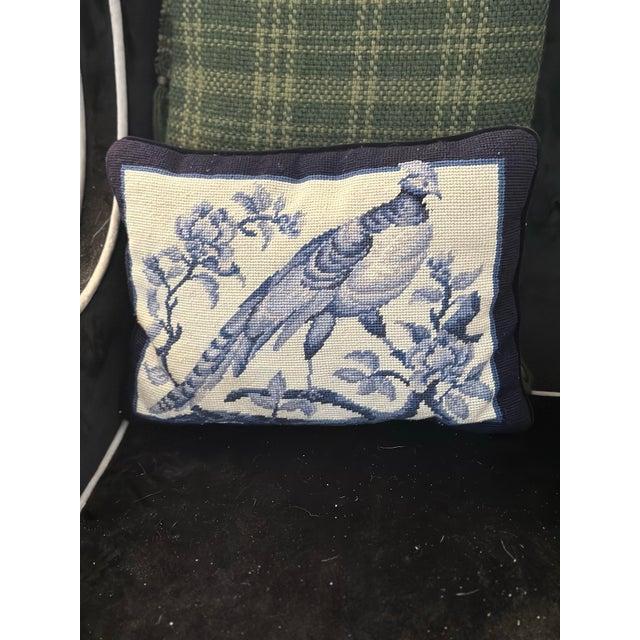 Brief description: Decorative needlepoint accent pillow featuring a blue pheasant perched among floral branches on a cream...