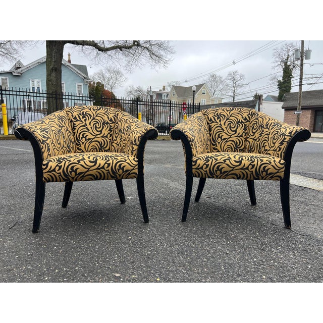 A stylish pair of upholstered barrel-style club chairs featuring a bold black and gold scroll pattern that adds instant...