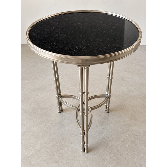 Elegant round accent table featuring a polished black marble top set waiting a silver-tone metal frame. the sculptural...