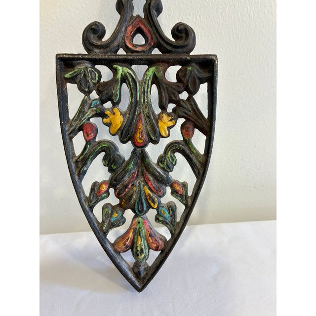 A charming vintage Wilton cast iron trivet featuring an intricate openwork floral and foliate design accented with traces...
