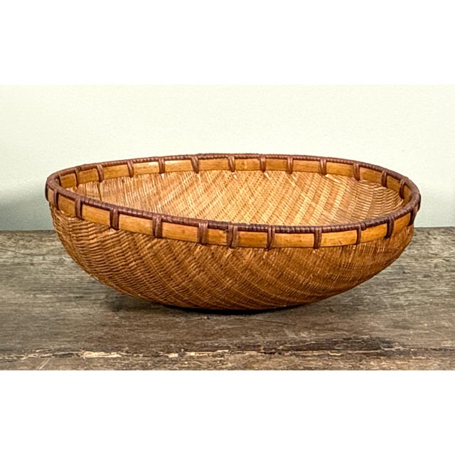 This handwoven winnowing basket, designed for washing and sorting rice and grain, features a shallow oval form constructed...