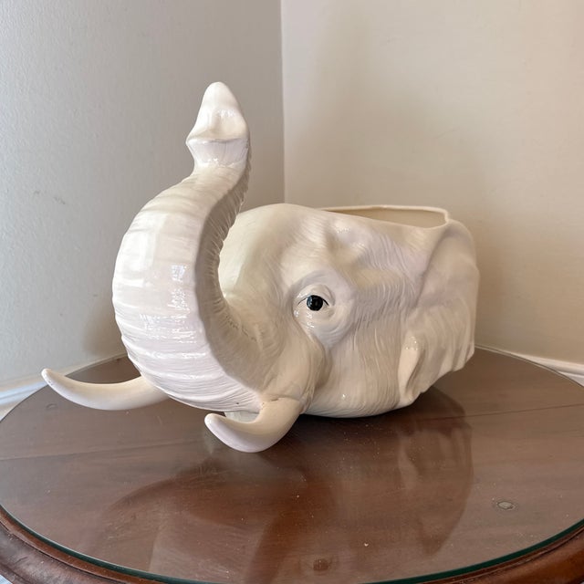 This is a striking ceramic planter in the shape of an elephant’s head, finished in a creamy off-white glaze. The elephant...