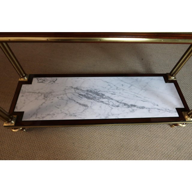 A console table with brass bands, a drawer in the frieze, and two tops in white and gray marble. The upper top is...
