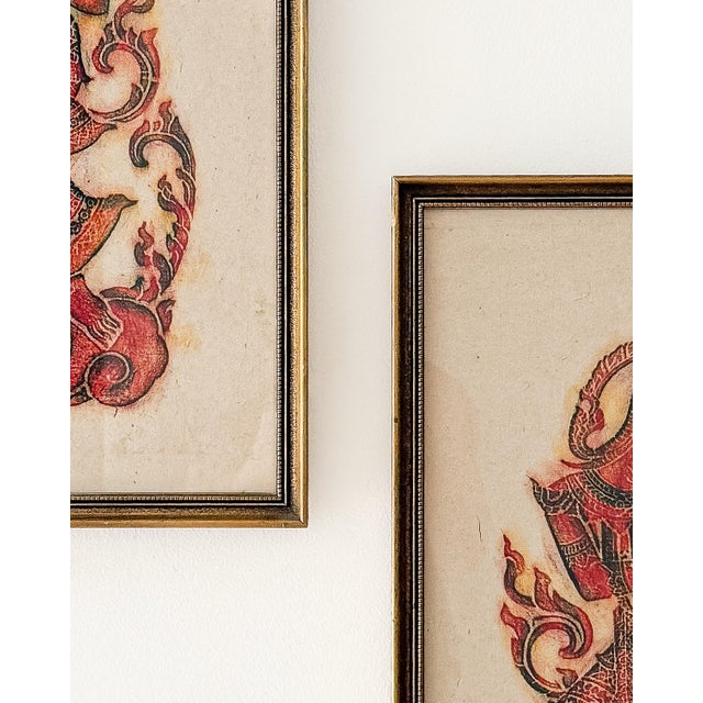 A decorative pair of framed Thai/Southeast Asian rubbing-style wall art pieces featuring classical figure imagery in rich...
