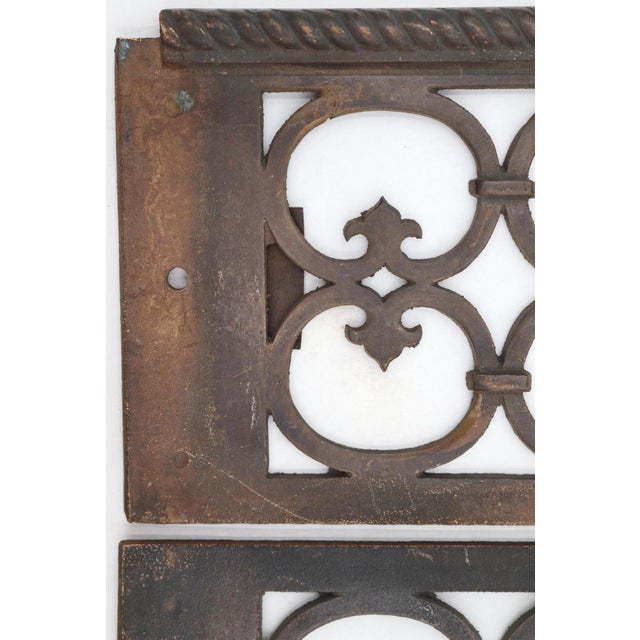 Reclaimed bronze wall register grills with a dark patina. They feature a repeating, interlocking circular fleur de lis...
