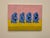 In this piece, a procession of pixelated blue figures—each caught mid-thought—sits against a split field of pink and...