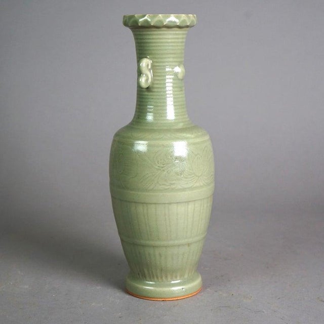 An antique Chinese vase offers art pottery construction with double scroll form handles, incised decoration and celadon...