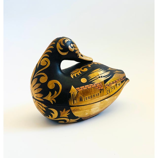 A vintage wood box in the shape of a duck. An intricately carved design of a village decorates the exterior of the box....
