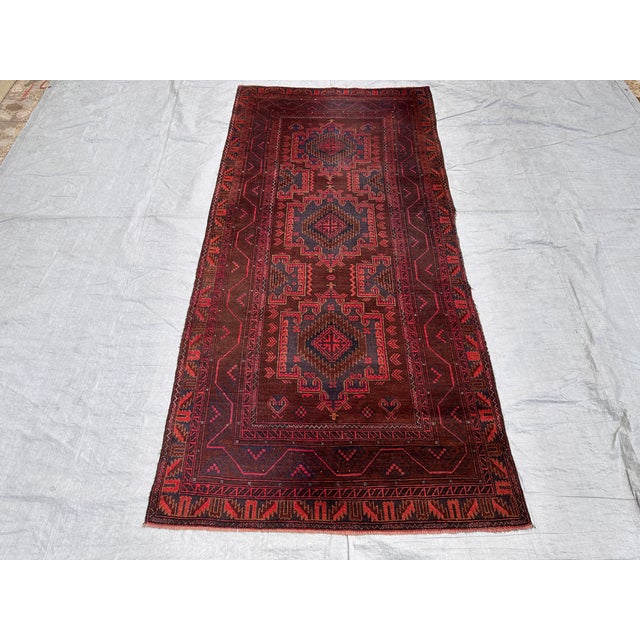 This antique hand-knotted Baluch rug features three stacked diamond medallions in deep navy and rust, each centered with a...