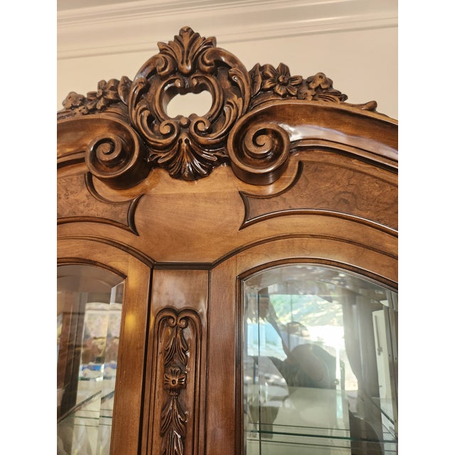 Elegant Italian wood curio cabinet has a rich brown finish with intricate floral and scrollwork carvings on the crown and...