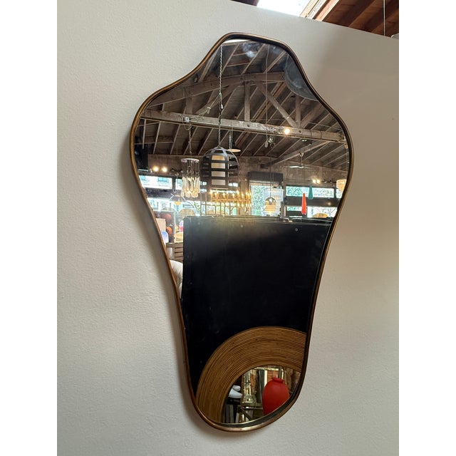 Elegant Italian wall mirror featuring a slender brass frame and an organic, asymmetrical silhouette. Its softly curved...