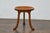 An English Liberty & Co. walnut Thebes stool from the Turn of the Century with tripod base. In-curving wooden seat resting...