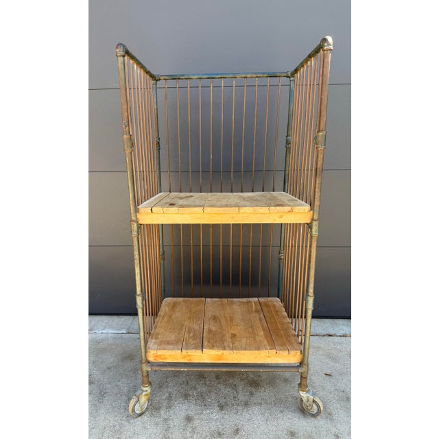 Vintage industrial two-tier bindery cart with metal frame and removable wood shelves and swivel casters. The metal frame...
