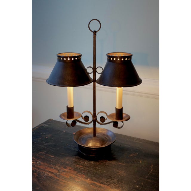 A sculptural double-arm table lamp in darkened forged iron, fitted with pierced conical tole shades and candle-style...