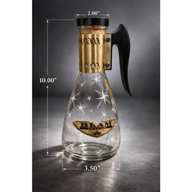 A striking mid-century Jim Beam glass carafe featuring classic atomic starburst etching, original brass collar, and...