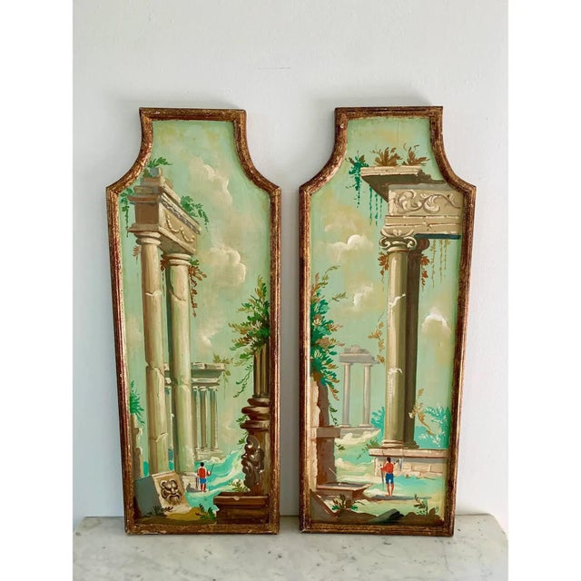 A distinctive pair of Italian capriccio landscapes, painted in oil on shaped panels and presented in softly worn giltwood...