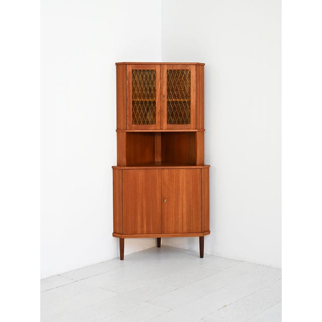 Teak veneered corner cabinet with a lower section featuring two doors and a top with decorated glass doors. 1950s. This...