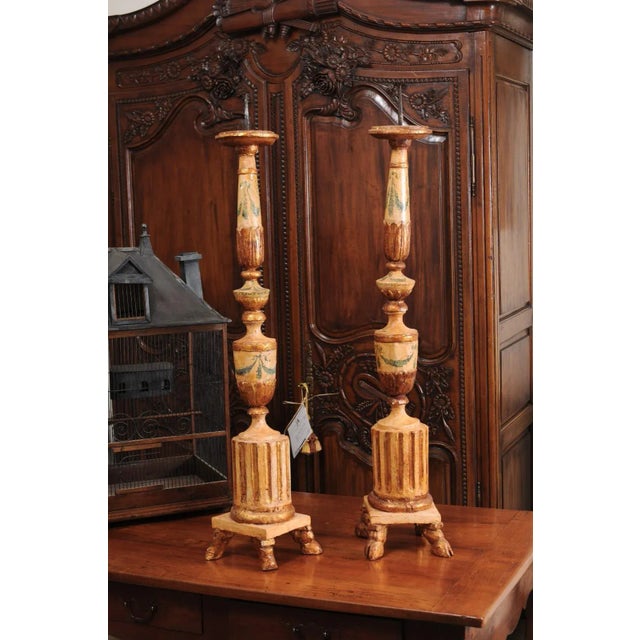 A pair of Italian neoclassical period painted and gilded candlesticks from the 18th century, with fluted motifs and hoof...