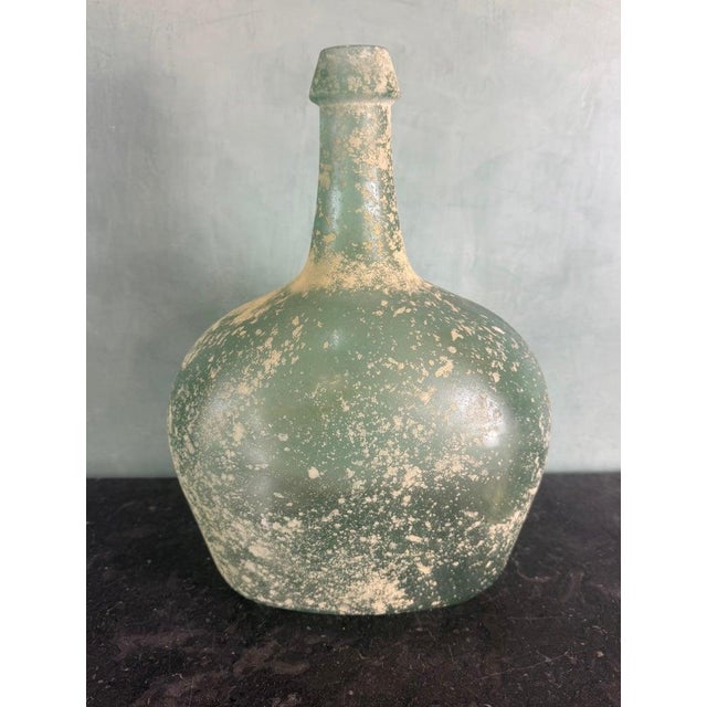 A beautifully hand-blown glass vase from Spain, distinguished by its sculptural, decanter-like silhouette and softly...