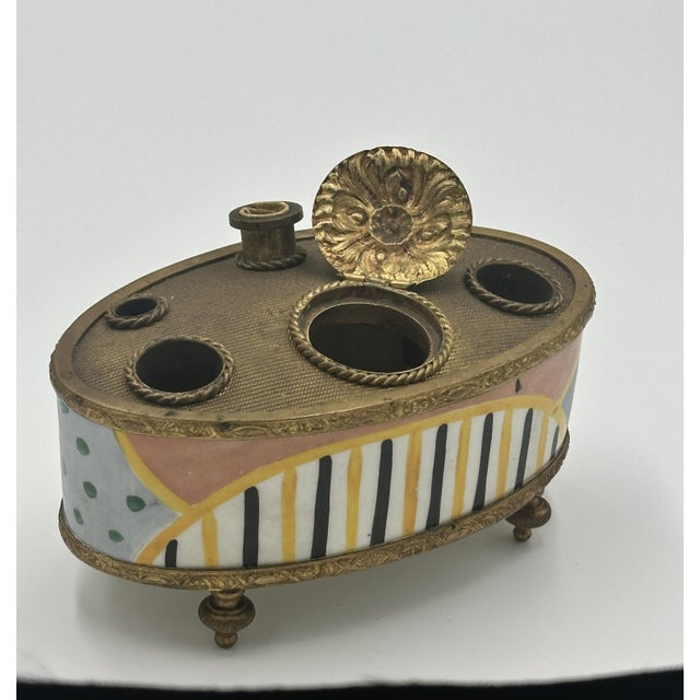 A beautifully detailed antique inkwell featuring a gilt metal top with multiple openings for pens and tools, a decorative...