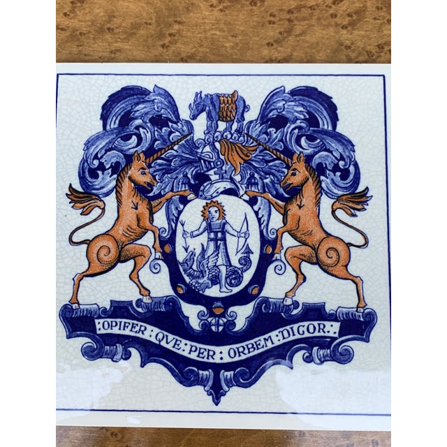 A classic Dutch Delft-style hand painted blue and white porcelain tile featuring an intricately rendered heraldic coat of...