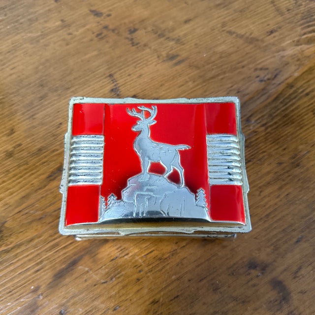 This striking vintage metal box captures attention with its intricate stag motif, beautifully framed by bright red accents...