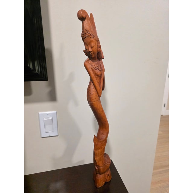 A towering, exceptionally elegant mid-century Balinese modernist sculpture depicting a graceful temple maiden standing...