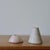 Minimalist candleholders carved from pale stone, one conical and one dome-shaped. Understated yet sculptural, with soft...