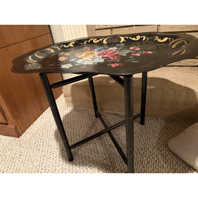 Vintage tôleware tray table, which features a hand-painted floral metal tray resting on a folding black faux-bamboo base....