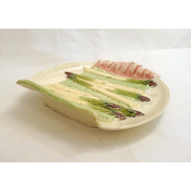 Oval asparagus serving dish with a trompe l'oeil design of folded floral tea towel fabric and asparagus arranged on top;...