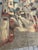 Vintage decorative tapestry featuring a charming European village street scene. The artwork depicts narrow cobblestone...