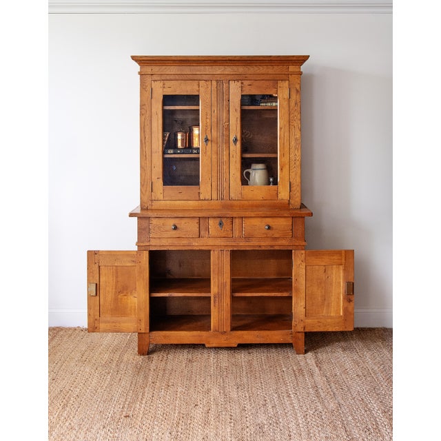Substantial rustic pine stepback cupboard, featuring glass-front upper cabinet doors, paneled lower storage, and warm...