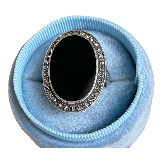 A ring that speaks in hushed elegance—the inky depths of polished onyx, framed by a constellation of glittering...