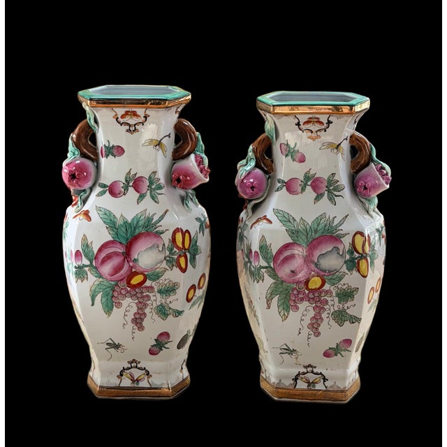 Beautiful matched pair of vases featuring vibrant fruit and floral motifs with dimensional sculptural pomegranate handles....