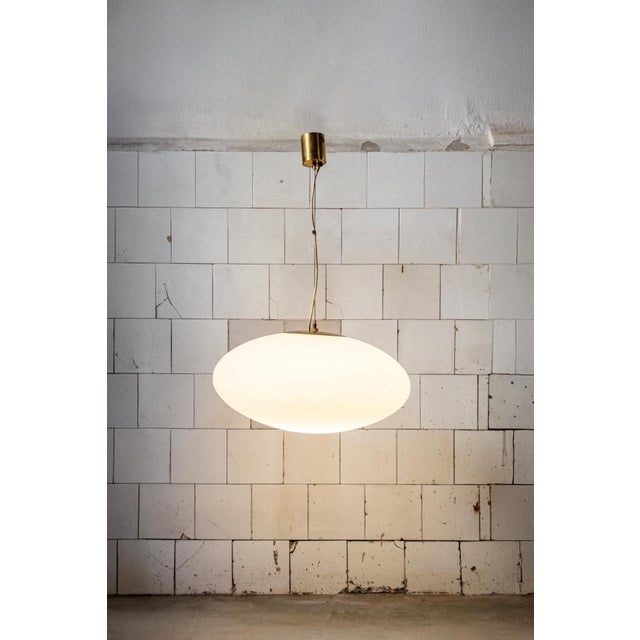 Pendant lamp with brass frame and white opal glass shade. Model 1104 Manufacturer Stilnovo 1960s This piece has an...
