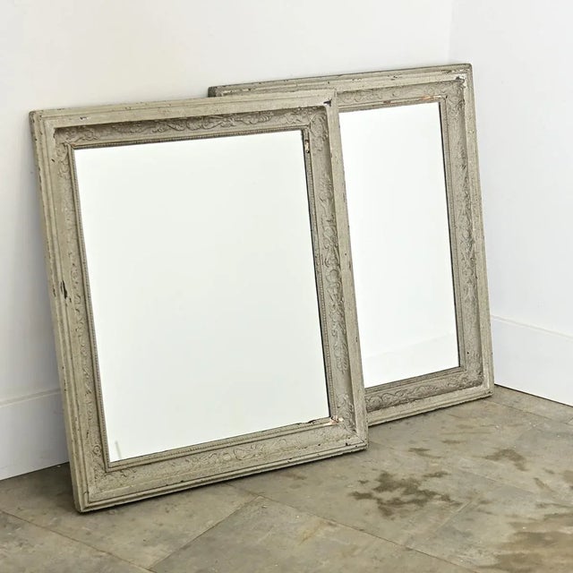 A lovely pair of French 19th century wall mirrors with delicate Neoclassical, scrolled motifs embossed in the recessed...