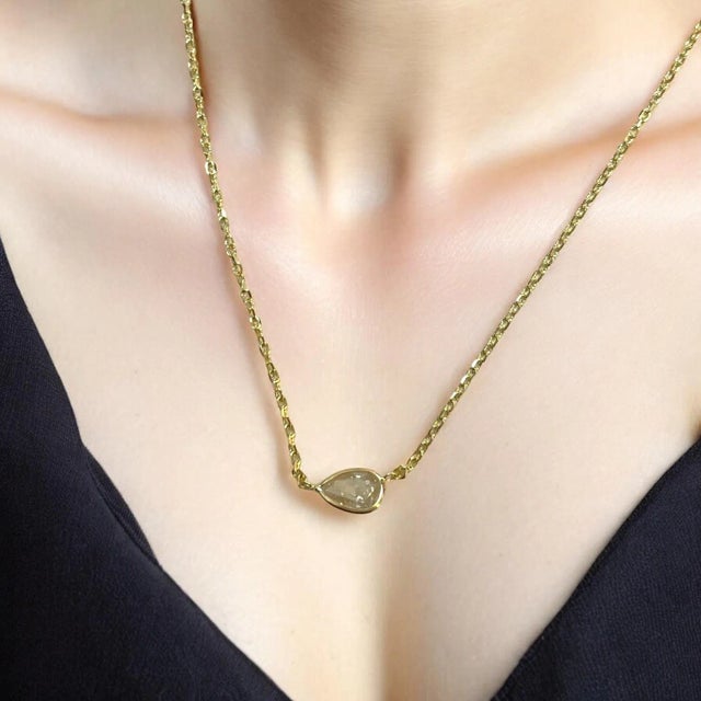 A delicate marvel, this necklace features a 0.73ct natural pear diamond bezel-set in radiant 14K yellow gold. The...