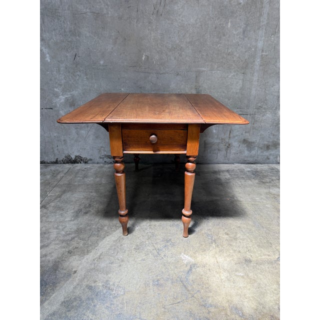 A warm, useful antique American one-drawer drop-leaf table, mid-19th century. The rectangular center section carries two...