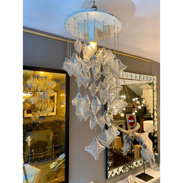 An unusual flush mounted chandelier with hung glass enveloped shaped pieces suspended on chains and descending in a...