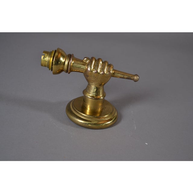 Brass wall sconce in the Art Deco hand-and-torch form, 1930s. A modeled clenched fist grips a fluted torch-form fitting,...