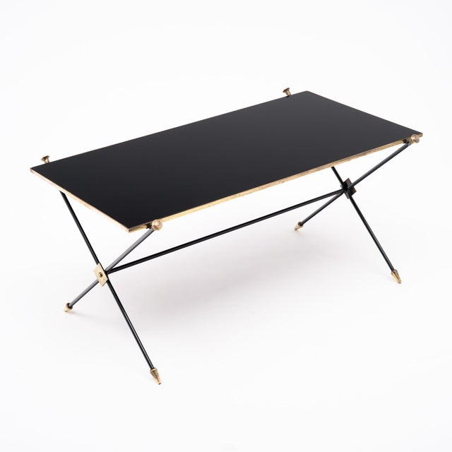 A sleek French mid-century coffee table combining a black glass top with a slender black metal frame and refined brass...