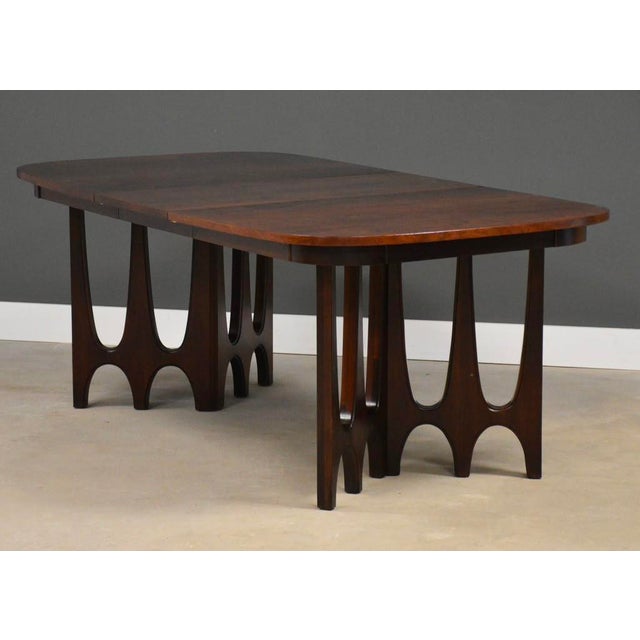A mid century modern walnut dining table with one 18” leaves which fully expand the table to 80.25” by Broyhill Brasilia....