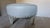 Two Dove grey round leather ottomans with modern square raised brass nailhead/rivet detail. Legs have rubbed subtle grey...